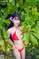 A woman in a red bikini posing in front of a bush.