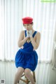 A woman in a blue dress and a red hat sitting on a stool.