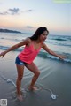 A woman in a pink tank top and denim shorts on the beach.