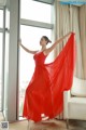 A woman in a red dress standing in front of a window.