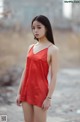 A woman in a red dress standing on a dirt road.