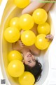 A woman laying in a bathtub filled with yellow balloons.