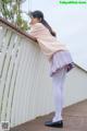 A woman in a pink sweater and purple skirt leaning against a fence.